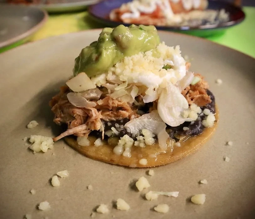 Sope de carnitas con frijoles, lechuga, queso y guacamole